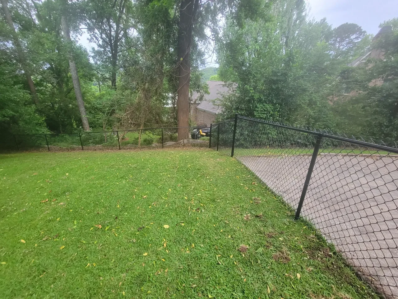 Black chain-link residential fence following sloped yard in Carlisle Alabama